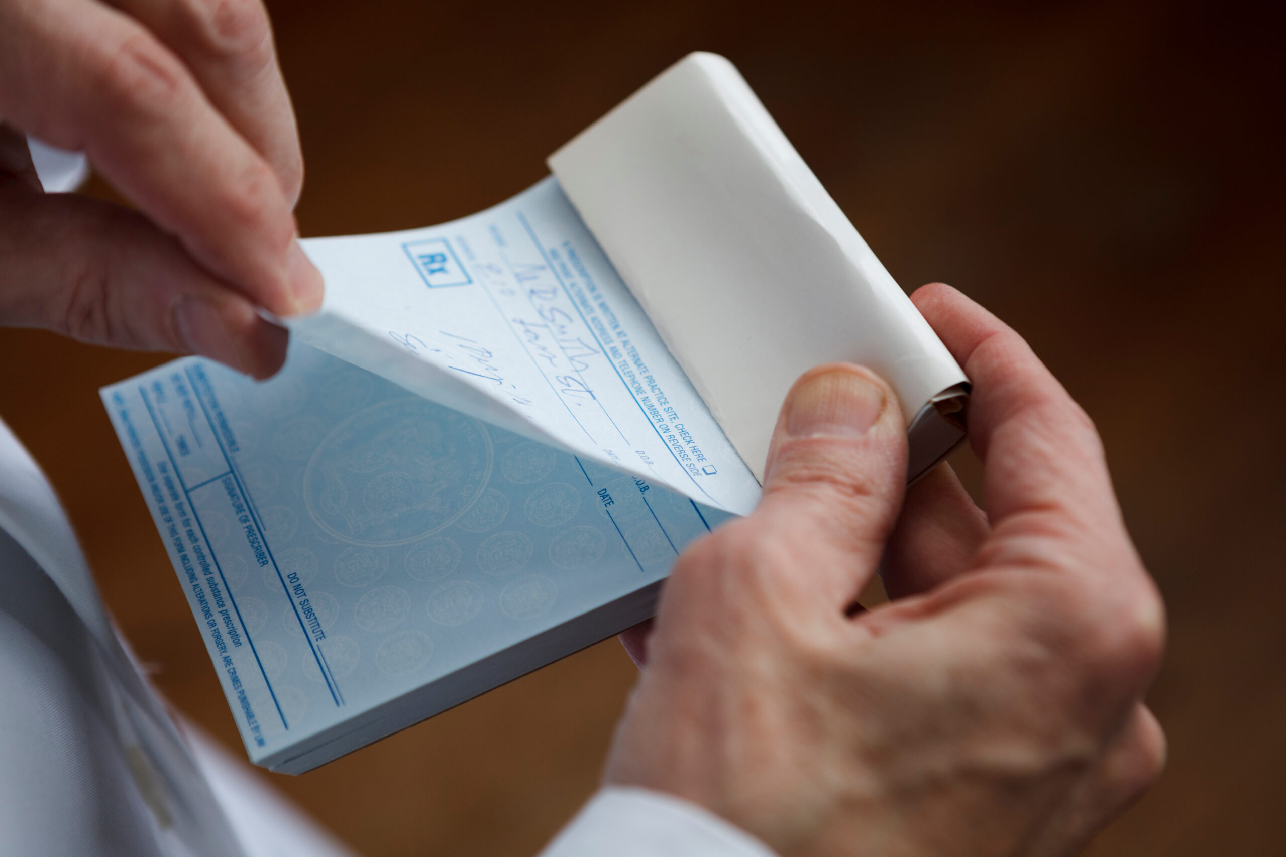 A doctor about to tear off a prescription from a prescription pad. NOTE TO INSPECTOR NO SENSITIVE INFORMATION HERE.