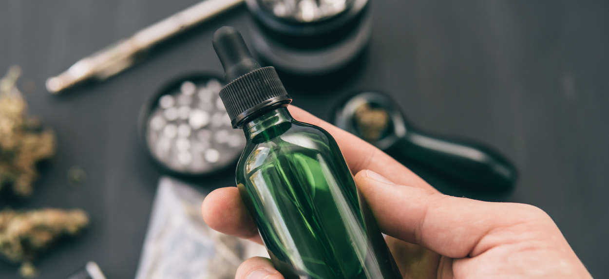 Person holding green bottle with marijuana accessories in background.