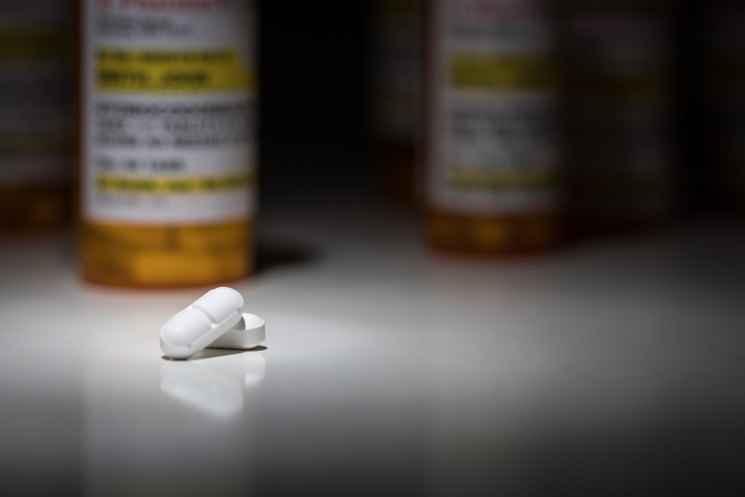White pills highlighted on a table with prescription bottles in the background