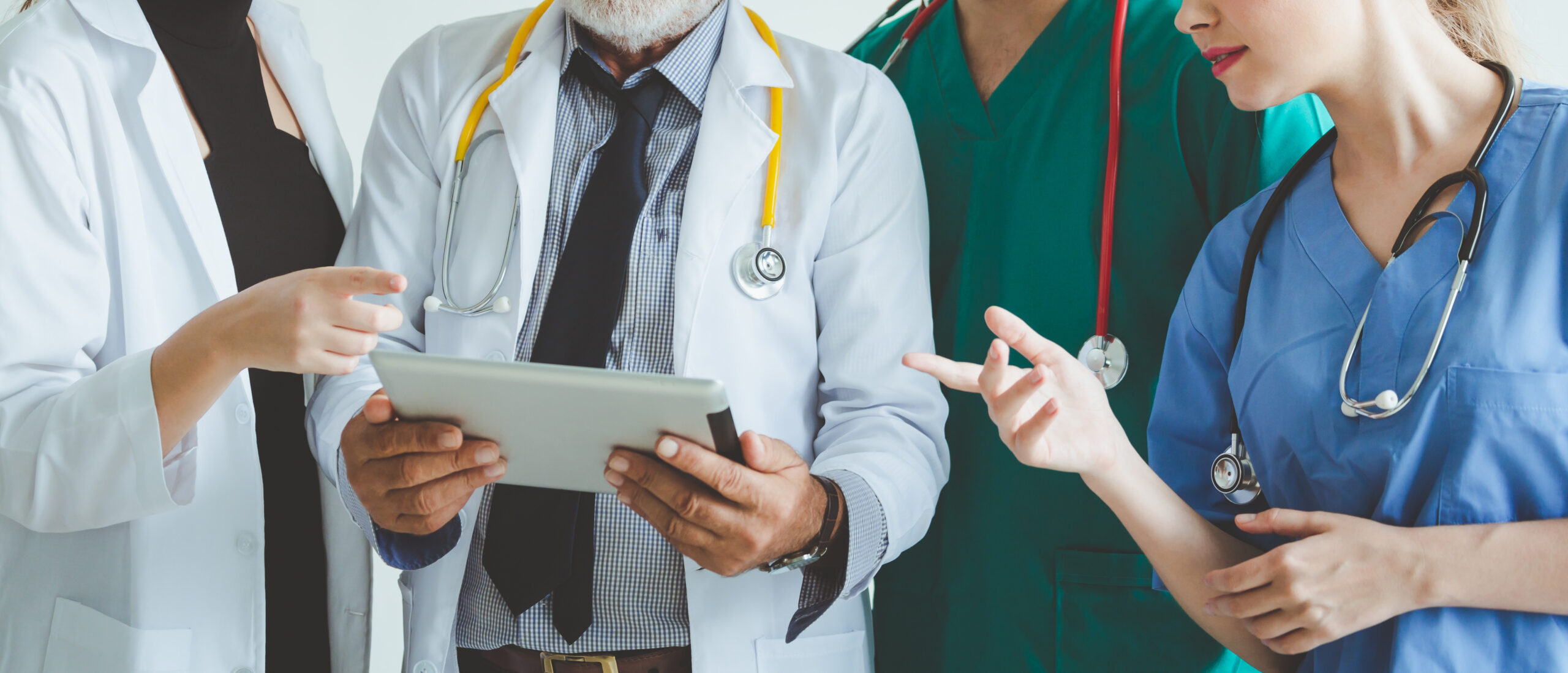 people wearing lab coats and scrubs with stethoscopes conversing around a chart