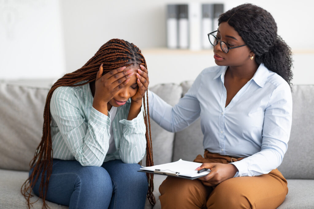 Woman with head in hands talking with female counselor whose hand rests on her shoulder