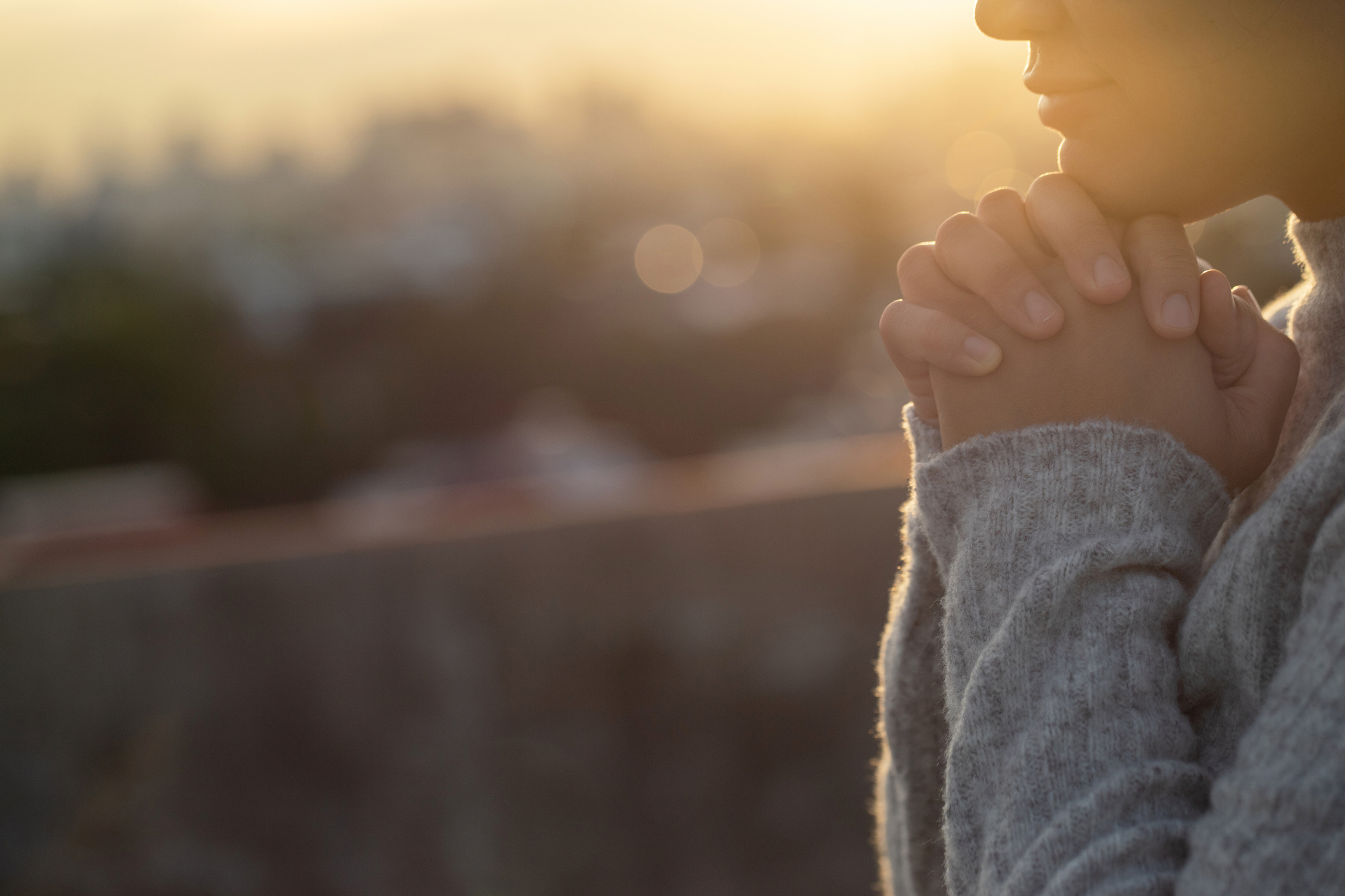 Woman in sunlight with hands clasped under chin