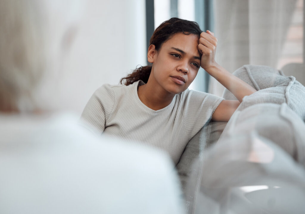 Woman on sofa leaning head on hand talking to someone in the foreground