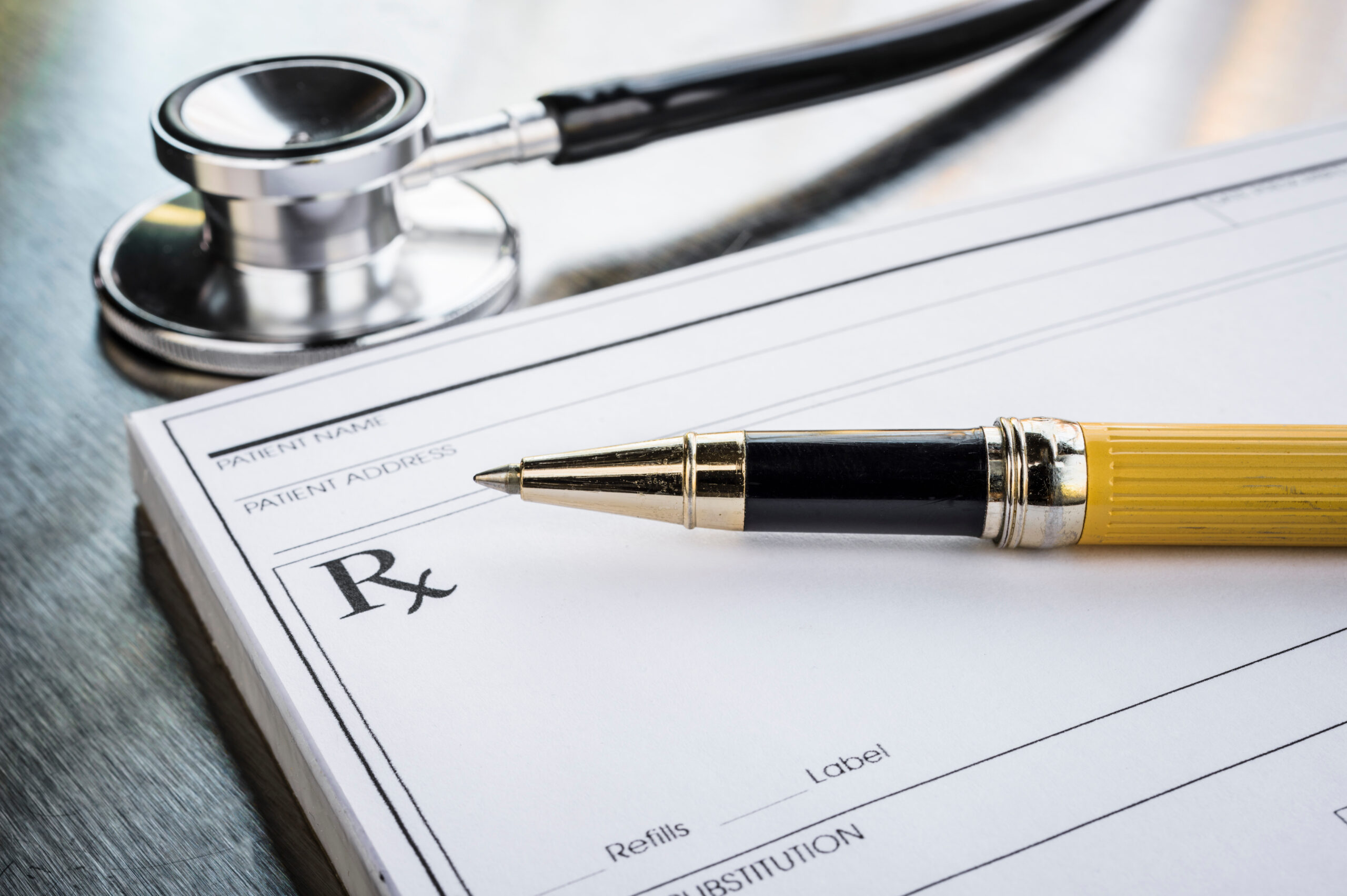 A doctors prescription pad with stethoscope sitting above it and a writing  pen sitting on top of it. 