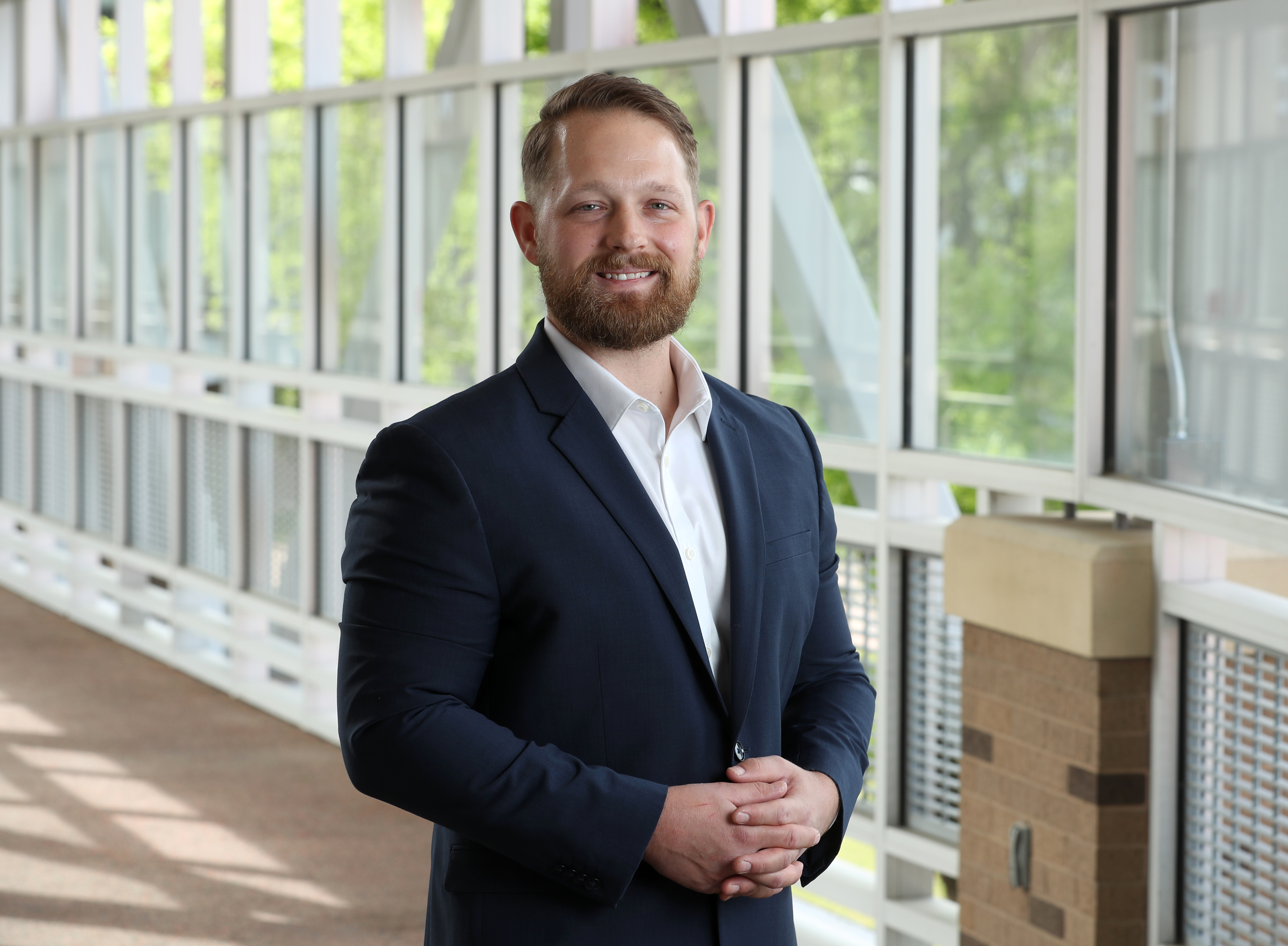 This is a picture of Craig Werner, Ph.D., associate director of neuroscience at the National Center for Wellness and Recovery (NCWR). He is standing in a lobby with windows behind him