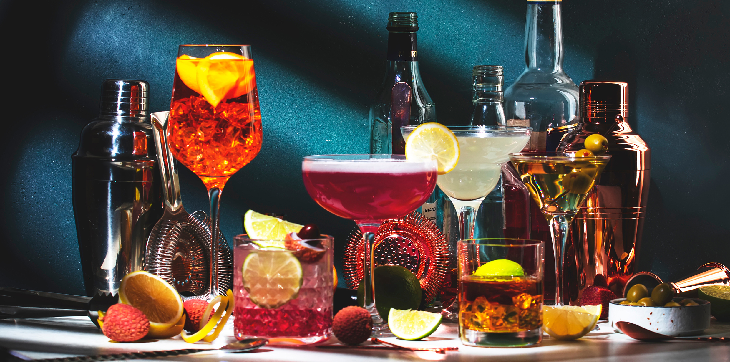 Alcoholic cocktails set, strong drinks and aperitifs, bar tools, bottles on dark green background, hard light. Martini vodka, pink lady, aperol spritz, margarita, old fashioned cocktail in glasses